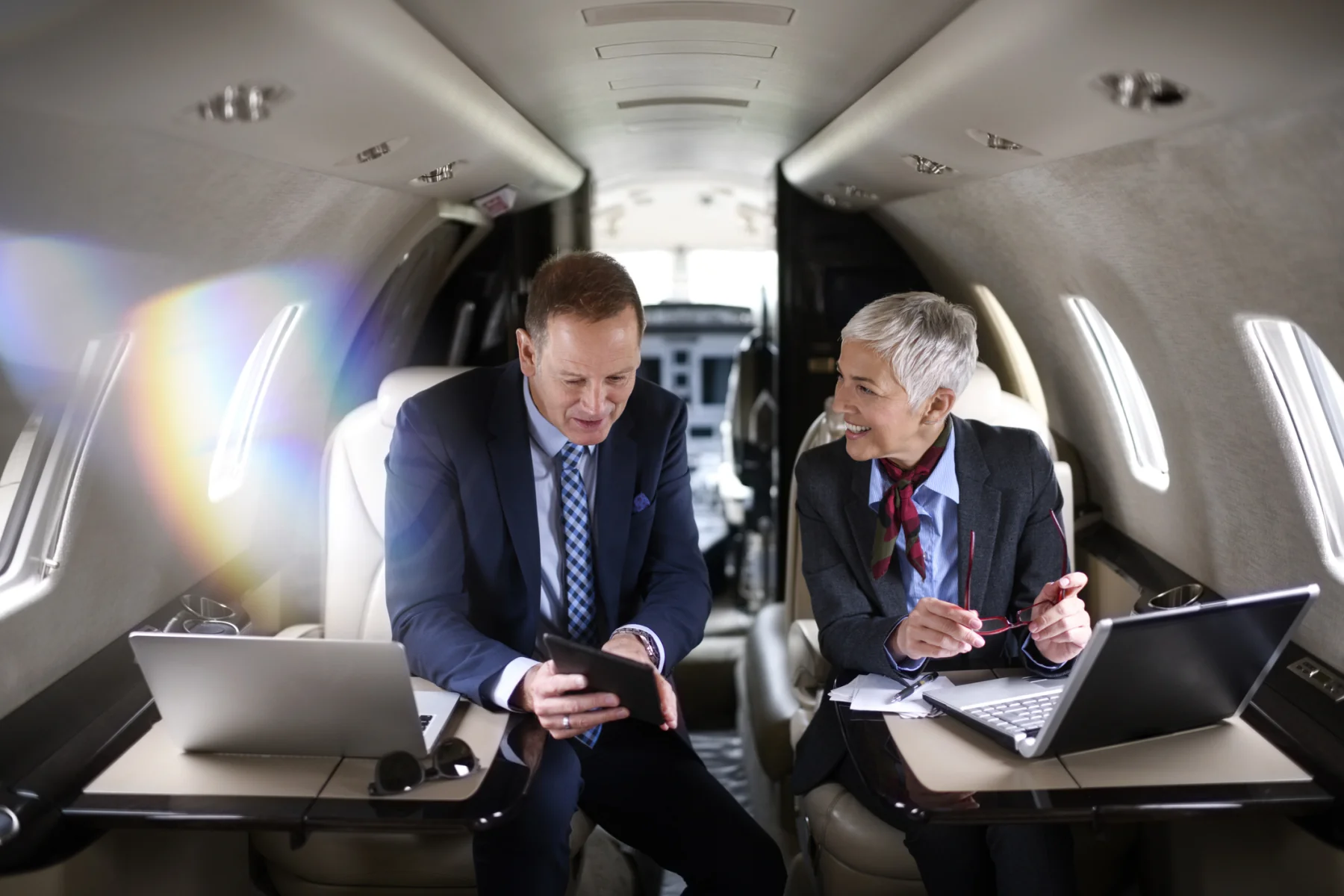 Zwei Geschäftsreisende besprechen ihre Arbeit mit Laptops und Tablet an Bord eines Privatjets