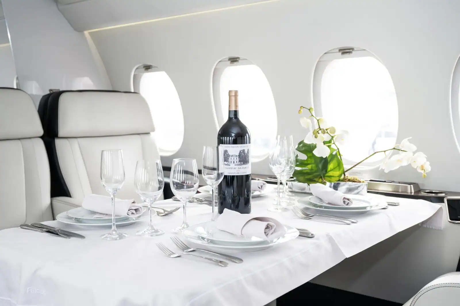 A dining table set with fine tableware, wine glasses and flowers aboard a private jet